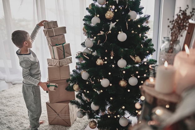 Menino empilhando presentes de natal ao lado de uma árvore de natal