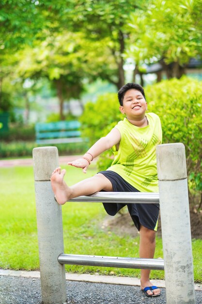 Menino esportivo asiático que se estende na barra de ferro no jardim