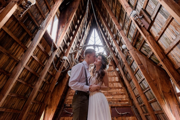 Foto grátis menino está beijando uma garota em chhek, vestida em trajes de casamento dentro de um edifício de madeira, casal apaixonado