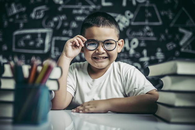 Menino estudando e segurando a perna de óculos em sala de aula.