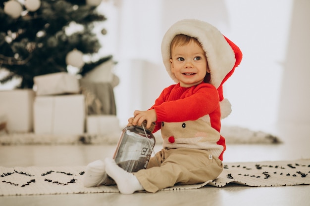 Menino fofo com chapéu de papai noel abrindo presentes no natal