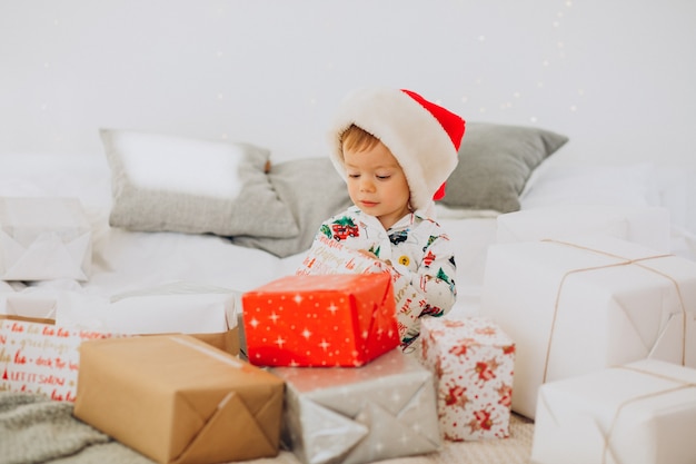 Menino fofo com chapéu de Papai Noel abrindo presentes no Natal