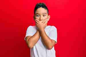 Foto grátis menino hispânico vestindo camiseta branca casual chocado cobrindo a boca com as mãos por engano. conceito secreto.