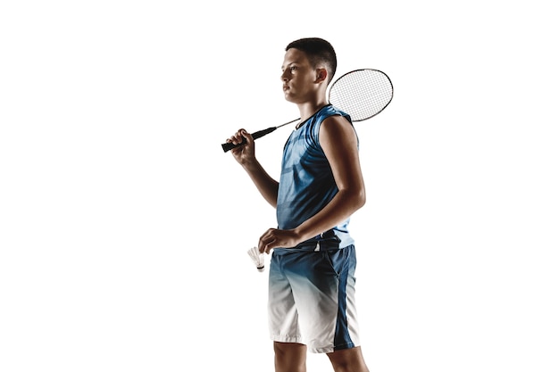 Foto grátis menino jogando badminton isolado no fundo branco do estúdio. jovem modelo masculino em roupas esportivas e tênis com a raquete em ação, movimento em jogo. conceito de esporte, movimento, estilo de vida saudável.