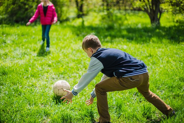 Menino jogando futebol com sua irmã no parque