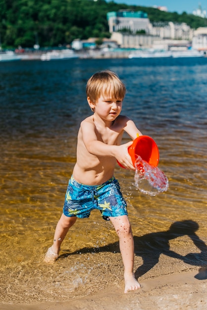 Menino jovem, em, shorts, despejar, água, ligado, mar, praia