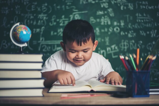 menino lendo um livro sentado à mesa na sala de aula