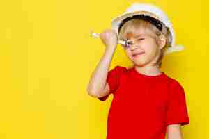 Foto grátis menino loiro adorável fofo em camiseta vermelha e capacete branco na parede amarela