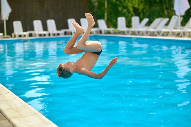 Menino no ar de cabeça para baixo acima da água da piscina