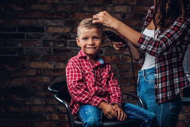 Menino pré-escolar bonito satisfeito cortando o cabelo. cabeleireiro de crianças com aparador está cortando garotinho na sala com interior loft.