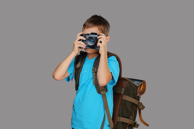 Menino pré-escolar tirando fotos com uma câmera fotográfica profissional. isolado em fundo cinza.