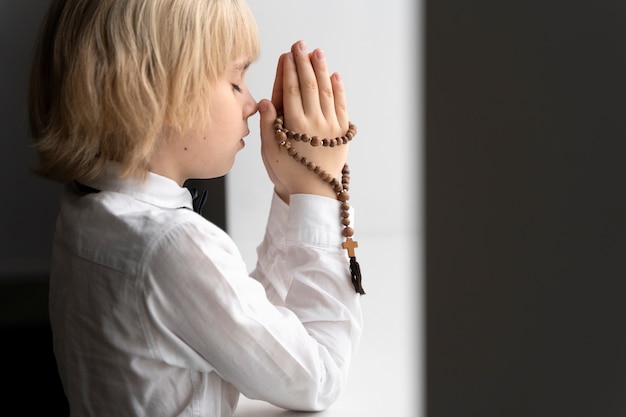 Foto grátis menino rezando com crucifixo plano médio