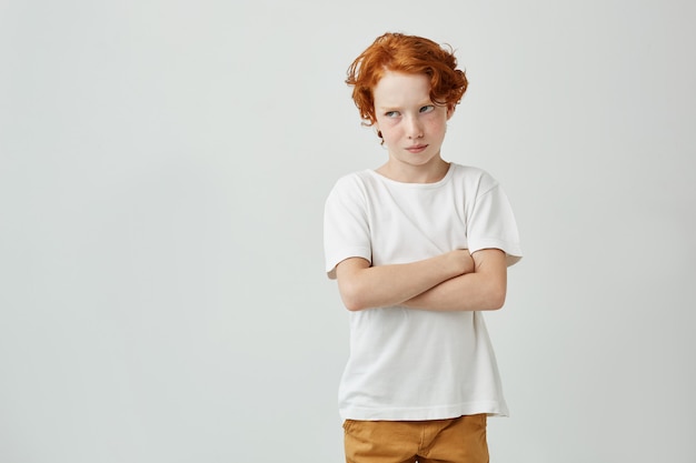 Menino ruivo lindo em t-shirt branca, olhando de lado sendo insatisfeito