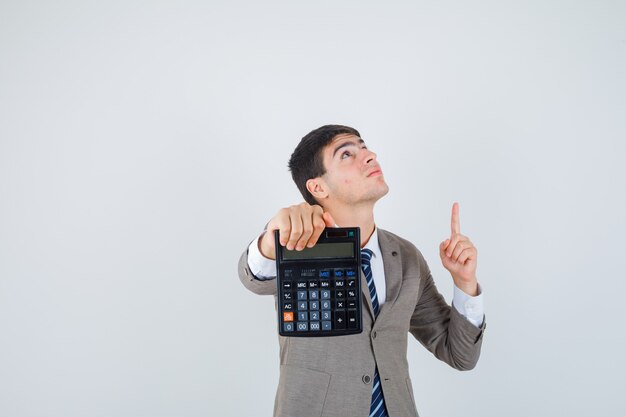 Menino segurando uma calculadora, apontando para cima com o dedo indicador em um terno formal