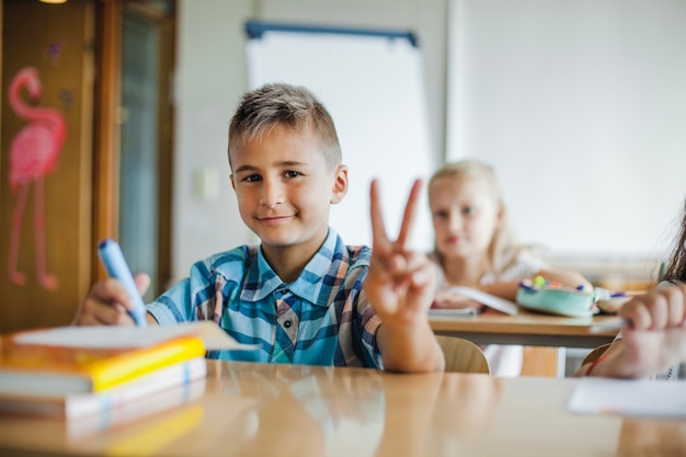 Menino sentado na mesa da escola gesticulando