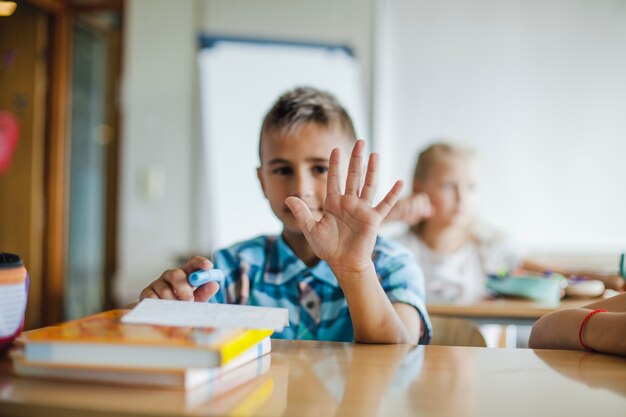 Menino sentado na mesa da escola mostrando palma