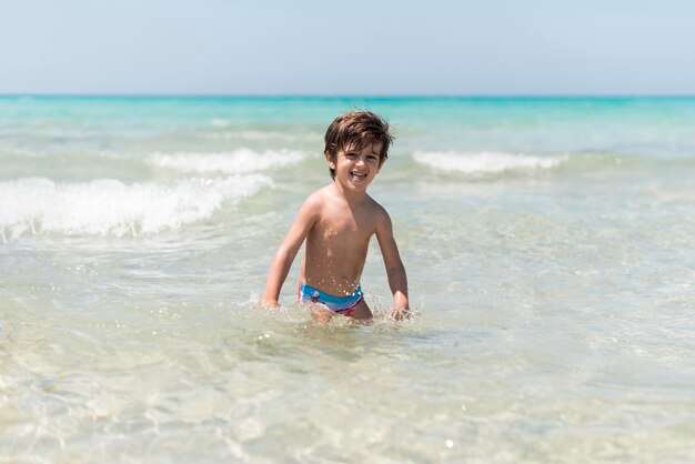 Menino sorridente brincando na água à beira-mar