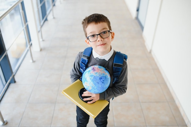 Menino sorridente feliz de óculos está indo para a escola pela primeira vez criança com mochila e livro na mão criança dentro da sala de aula de volta à escola Foto Premium