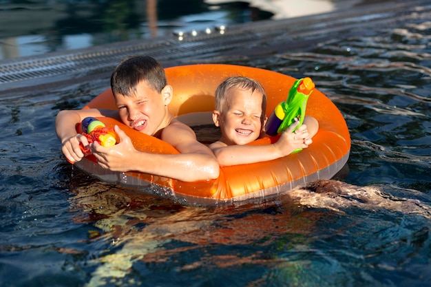 Meninos se divertindo na piscina com boia e pistola d'água