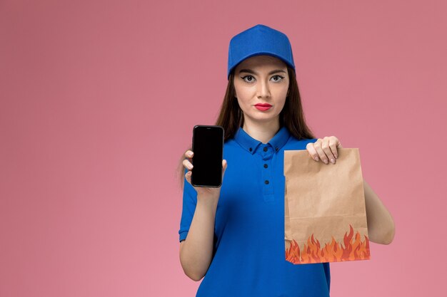 Mensageira de frente com uniforme azul e capa segurando o telefone e o pacote de comida na mesa rosa