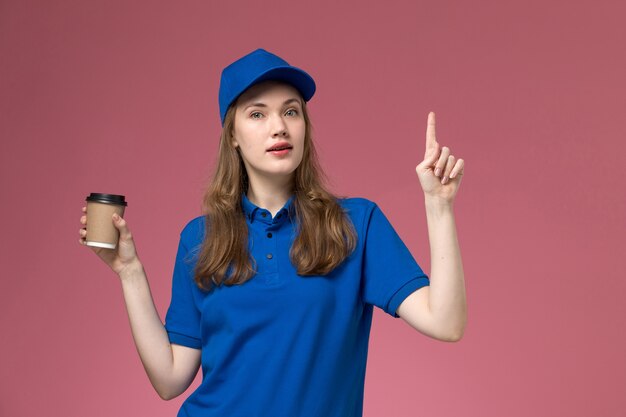 Mensageira de frente com uniforme azul segurando uma xícara de café marrom com o dedo levantado na empresa de entrega de uniforme rosa claro