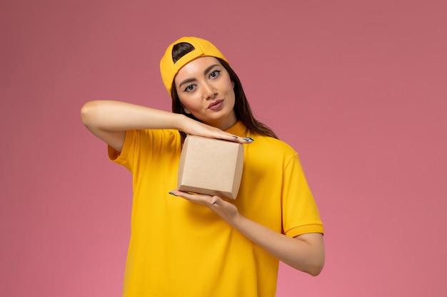 Mensageira de frente feminina em uniforme amarelo e capa segurando um pequeno pacote de entrega de comida em uniforme rosa claro garota de empresa de entrega de serviço