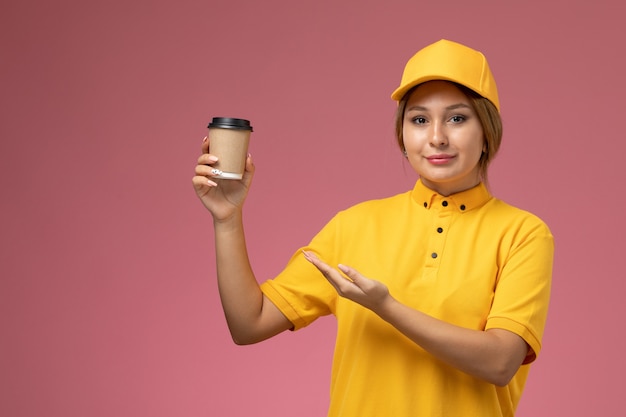 Mensageira de frente para mulher com capa amarela uniforme segurando xícara de café de plástico na cor de trabalho de entrega uniforme de fundo rosa