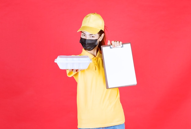 Mensageira de uniforme amarelo e máscara preta segurando um pacote para viagem e apresentando a lista de assinaturas