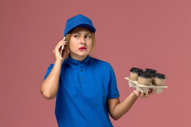 mensageira de uniforme azul falando no telefone e segurando xícaras de café marrons na entrega de uniforme de serviço de trabalho rosa claro