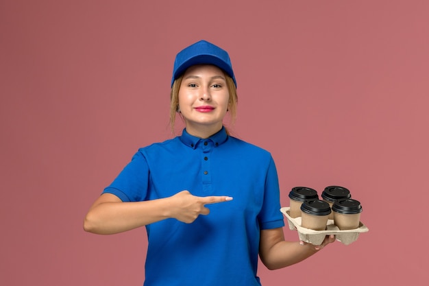 mensageira de uniforme azul segurando xícaras de café marrom com um sorriso rosa, serviço de entrega uniforme de trabalhador