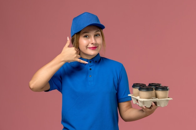 mensageira de uniforme azul segurando xícaras de café marrons posando com um sorriso rosa, trabalhador de trabalho de entrega de uniforme de serviço