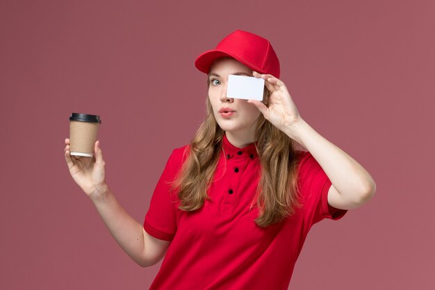 Mensageira de uniforme vermelho segurando café e cartão branco em rosa claro, entrega de trabalhador de serviço uniforme de trabalho