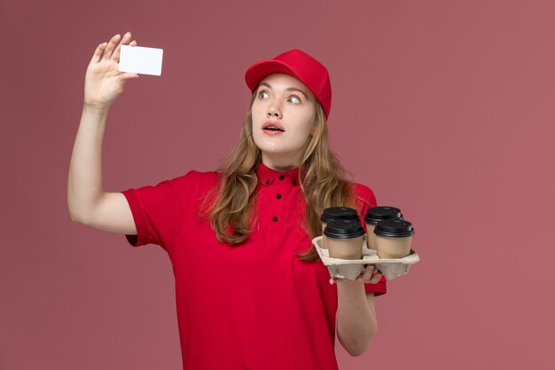 mensageira de uniforme vermelho segurando cartão e xícaras de café marrons no serviço de uniforme rosa