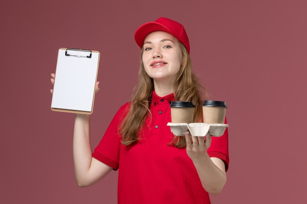 Foto grátis mensageira de uniforme vermelho segurando xícaras de café marrom e um bloco de notas rosa claro