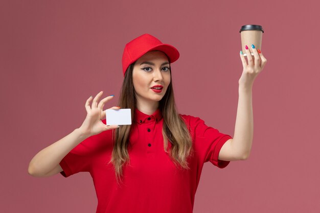 Mensageira feminina de uniforme vermelho e capa segurando a xícara de café de entrega com cartão branco no fundo rosa uniforme de entrega