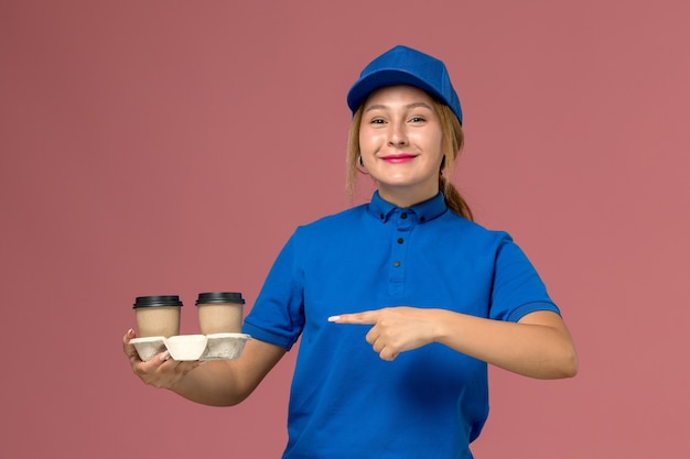 Mensageira feminina em uniforme azul posando e segurando xícaras de café com um sorriso na cor rosa, trabalho de entrega de uniforme de serviço