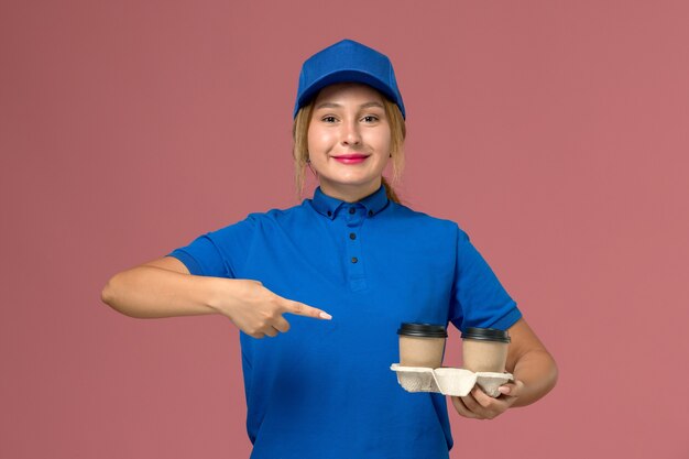 Mensageira feminina em uniforme azul posando segurando xícaras de café com um leve sorriso na rosa, trabalhador de trabalho de entrega de uniforme de serviço