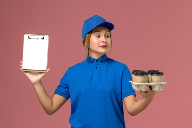 mensageira feminina em uniforme azul segurando um bloco de notas junto com xícaras de café marrom em rosa claro, entrega de uniforme de serviço de trabalho