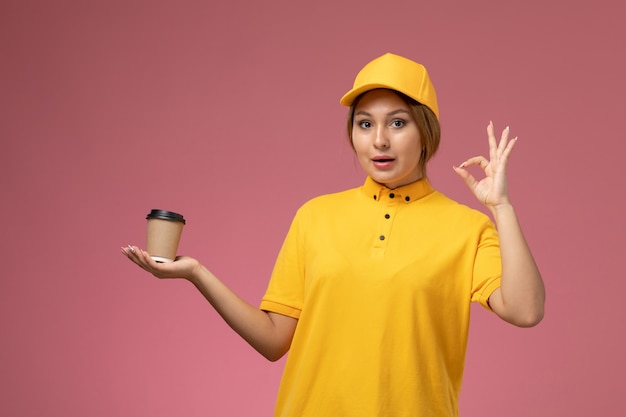 Mensageiro de frente com capa amarela uniforme segurando xícara de café de plástico marrom na mesa rosa uniforme cor feminina de entrega