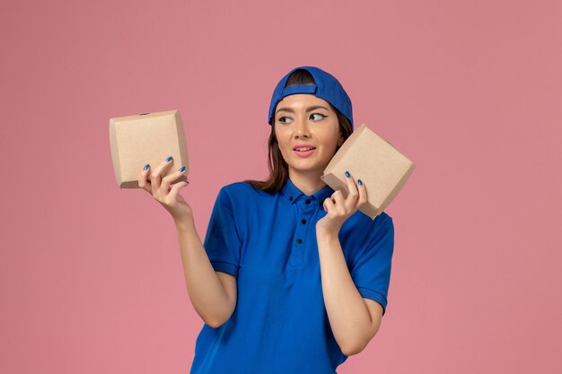 Mensageiro de frente com capa uniforme azul segurando pequenos pacotes de entrega na parede rosa claro, trabalho de entrega de funcionário de serviço