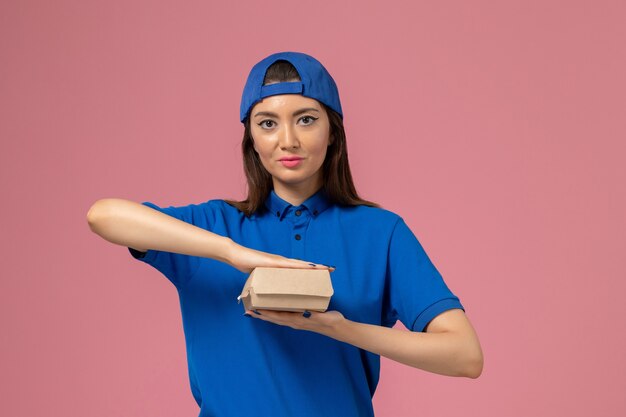 Mensageiro de frente com capa uniforme azul segurando um pequeno pacote de entrega na parede rosa, trabalho de trabalhador de entrega de serviço de funcionário