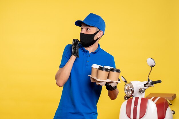 Mensageiro de frente com máscara preta segurando café em serviço de uniforme de trabalho cobiçado por uma pandemia de emprego amarelo