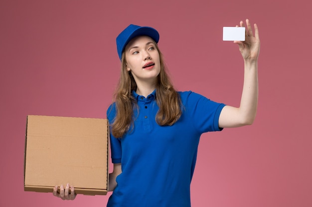Foto grátis mensageiro de frente com uniforme azul segurando uma caixa de entrega de comida e um cartão branco na mesa rosa.