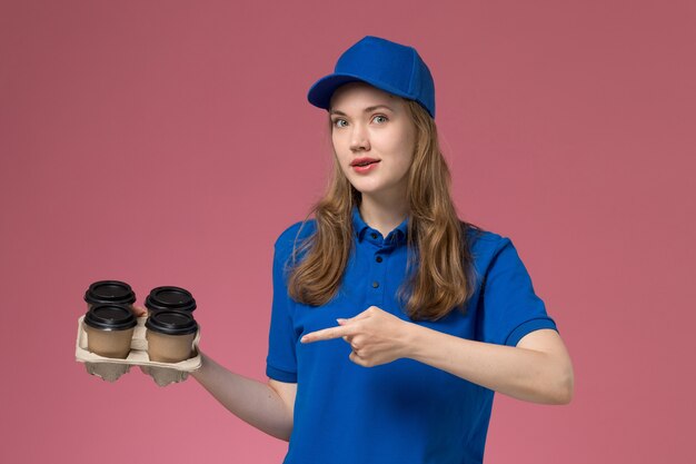 Mensageiro de frente com uniforme azul segurando xícaras de café marrom apontando na mesa rosa uniforme de serviço da empresa trabalhador