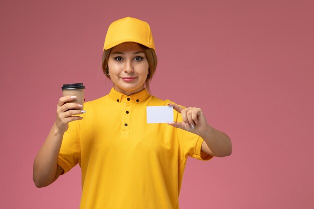 Mensageiro feminino de vista frontal em uniforme amarelo capa amarela segurando café e cartão na mesa rosa uniforme entrega de trabalho cor feminina