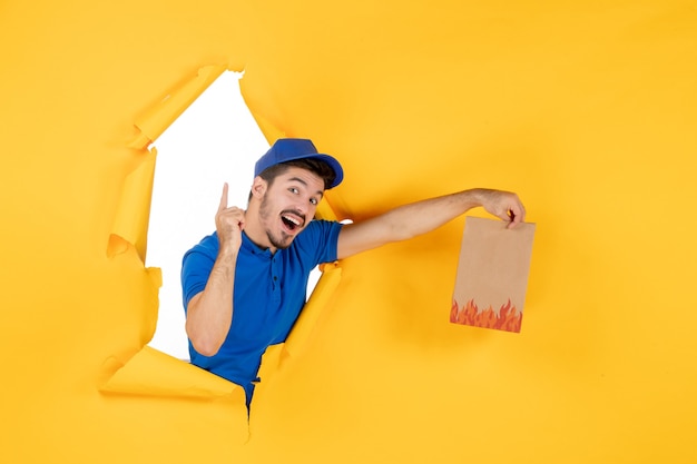 Mensageiro frontal masculino com uniforme azul dando pacote de comida no espaço amarelo