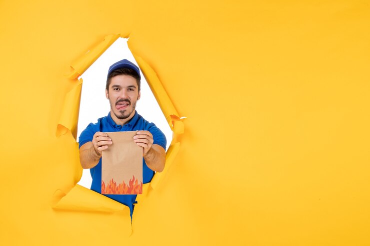 Foto grátis mensageiro frontal masculino com uniforme azul e pacote de comida no espaço amarelo