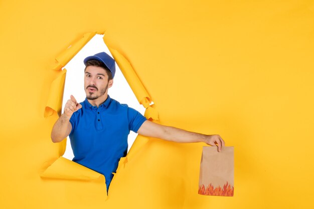 Mensageiro frontal masculino com uniforme azul segurando um pacote de comida no espaço amarelo