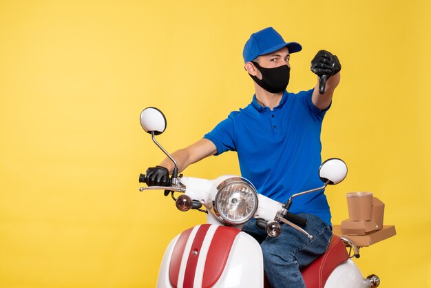 Mensageiro frontal masculino em uniforme azul e máscara descontente com o serviço de covidemia de trabalho amarelo - serviço de pandemia de entrega de bicicletas