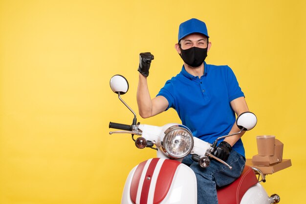 Mensageiro frontal masculino em uniforme azul e máscara regozijando-se com o vírus amarelo, trabalho covid, serviço de entrega, bicicleta pandêmica de trabalho